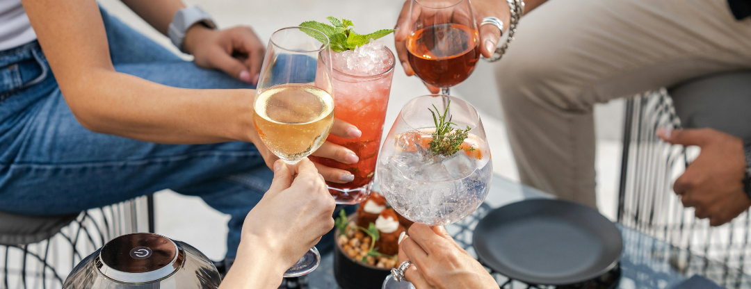 People toasting with glasses of wine and a cocktail at an outdoor gathering.